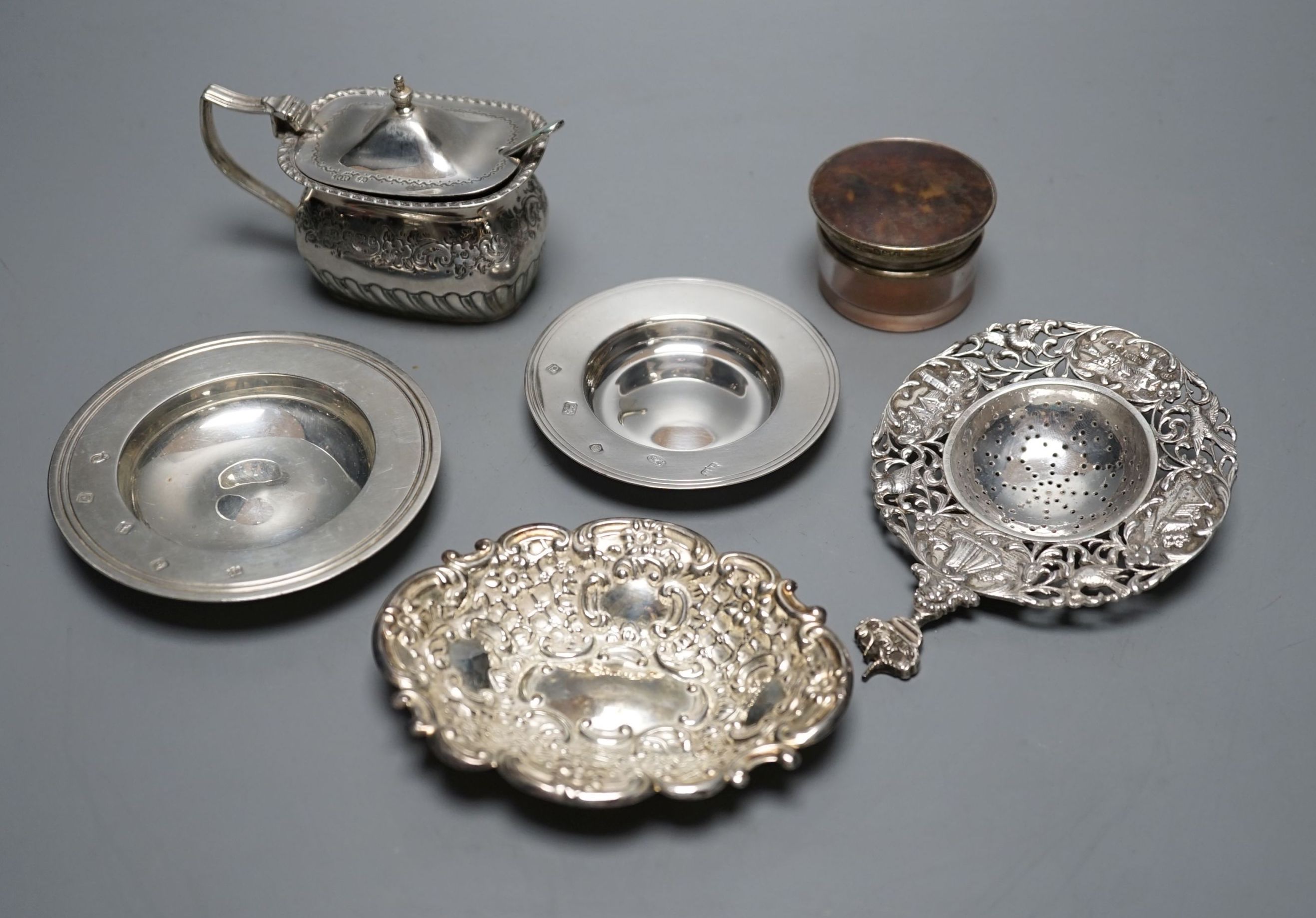 A late Victorian silver mustard, Sheffield, 1895, two small silver armada dishes, a silver bonbon dish, silver tea strainer(a.f.) and a silver mounted glass toilet jar.